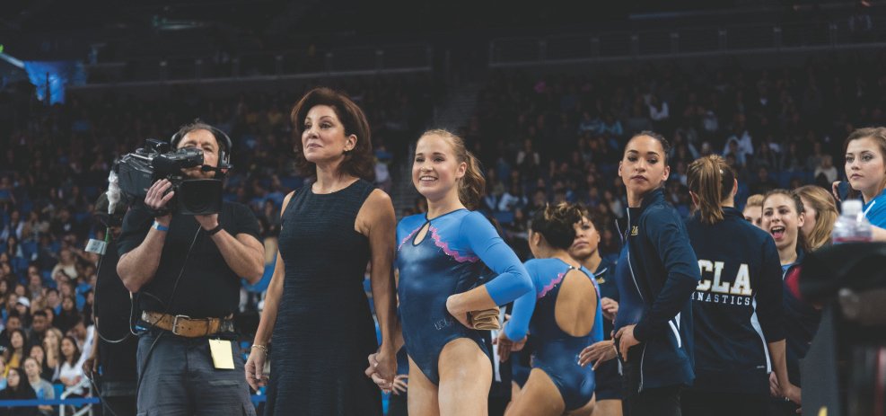 Coach Valerie Kondos Field standing proudly with her UCLA gymnastics team