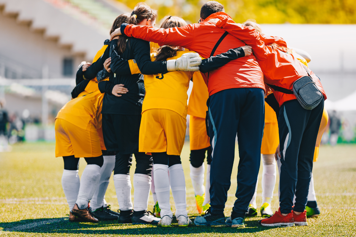 Coaches and youth team members in a huddle in an outdoor stadium.